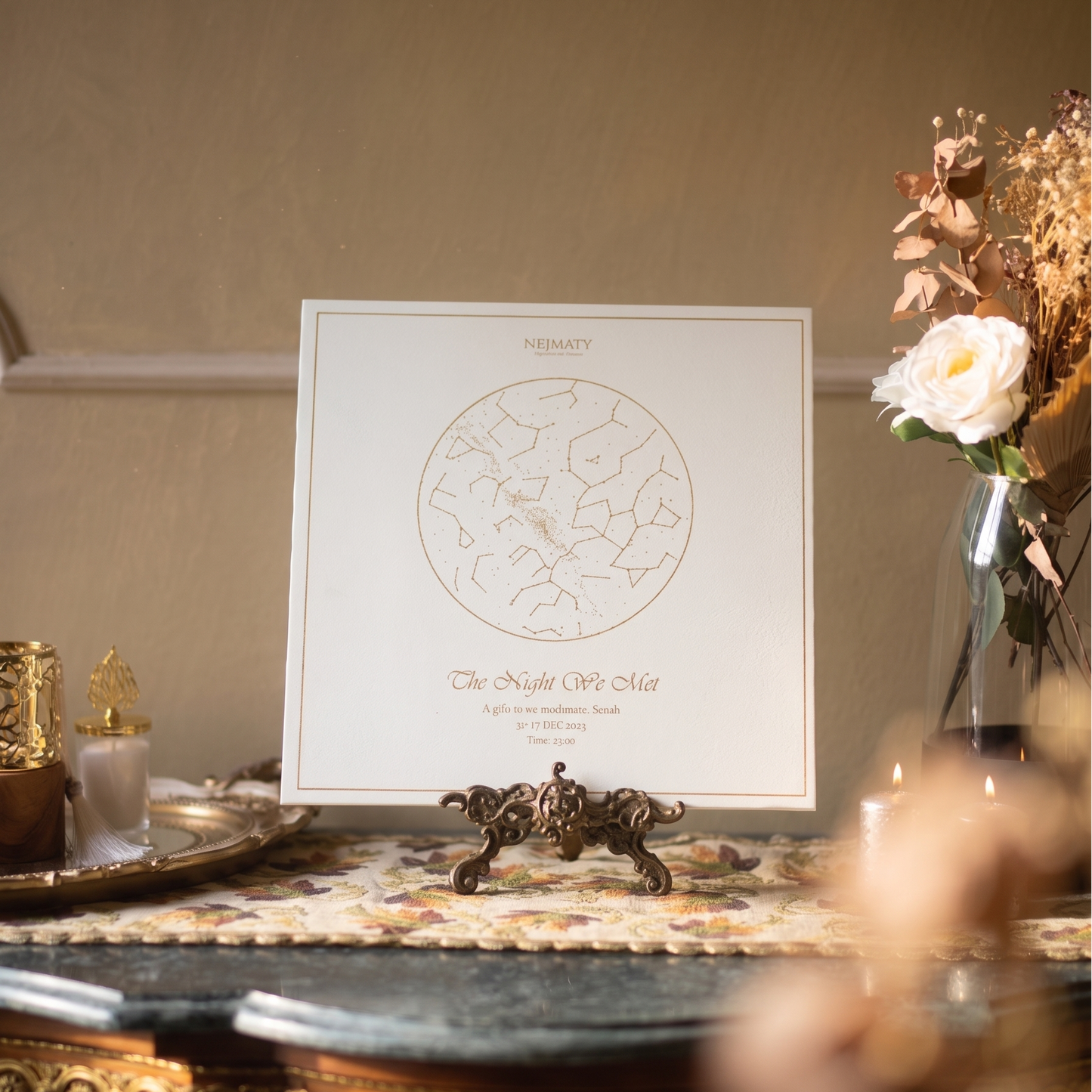 Decorative setting with a framed star map on a table, flowers, and candles.